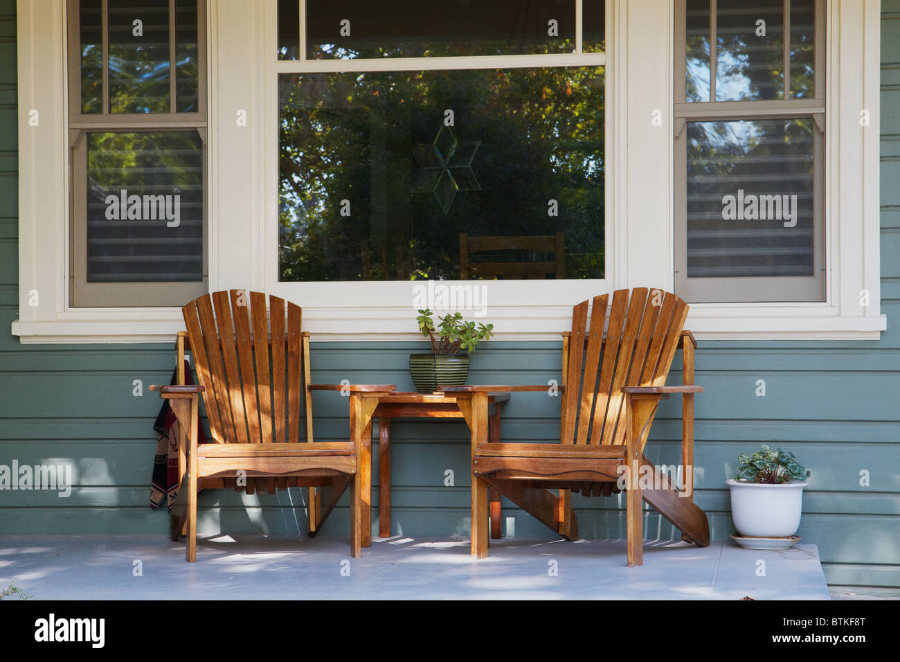 Two adirondack chairs on a porch with picture window background Stock