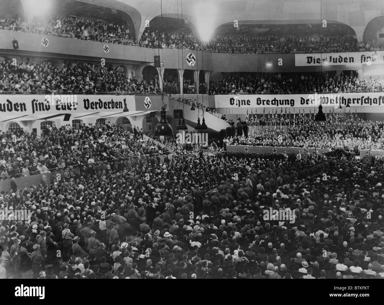 Anti-Semitic rally, with swastikas and anti-Semitic banners, at the massive auditorium of Sportpalast, Berlin, where Nazi propagandist, Julius Streicher, would speak on August 16, 1935. Within a month, Germany would adopt the Nuremberg Laws, stripping German Jews of their citizenship and civil rights. Stock Photo