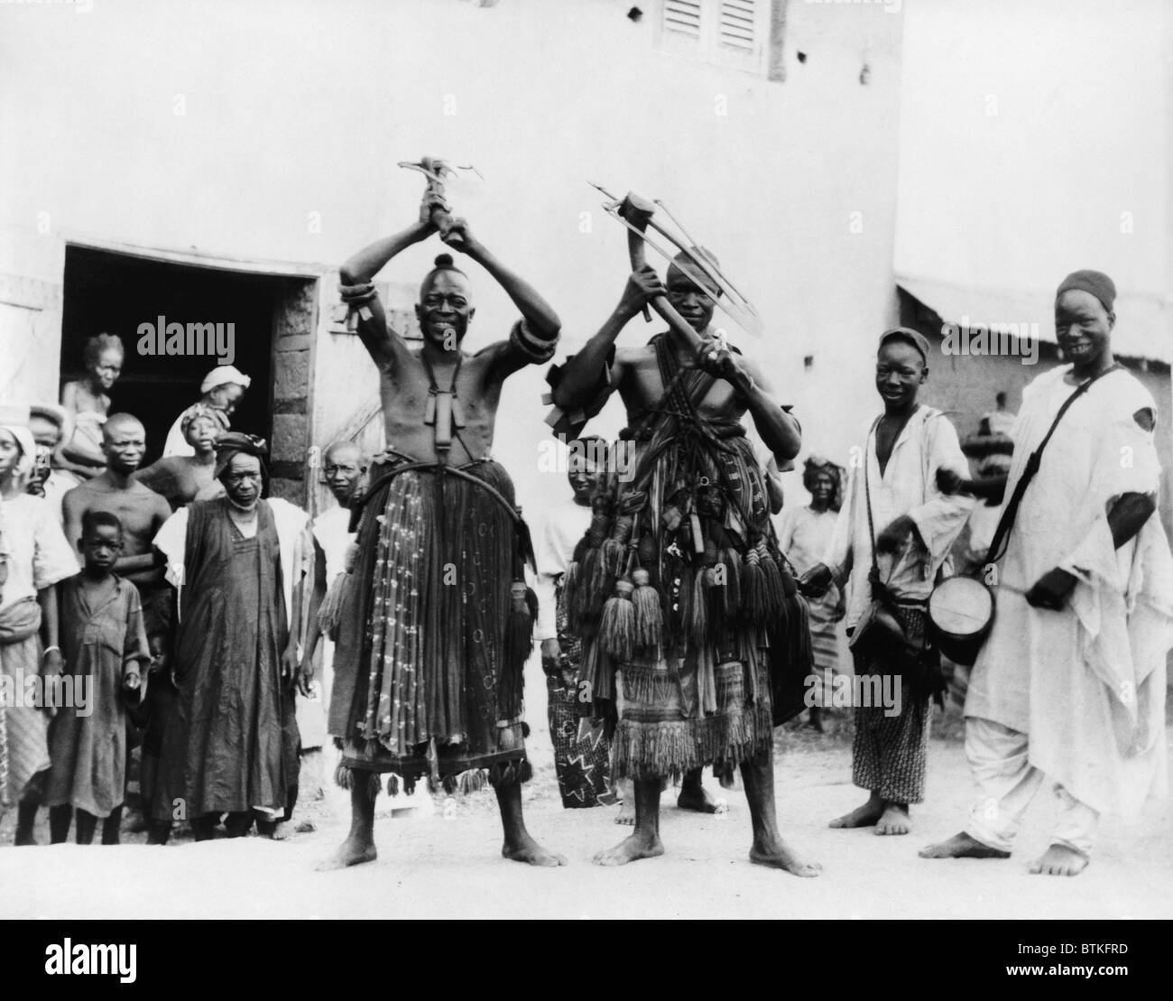 Two itinerant medicine men on a street in the village of Abeokuta, Southern Nigeria. Performing a 'hoe dance' a traditional Hausa agricultural dance. Ca. 1935. Stock Photo