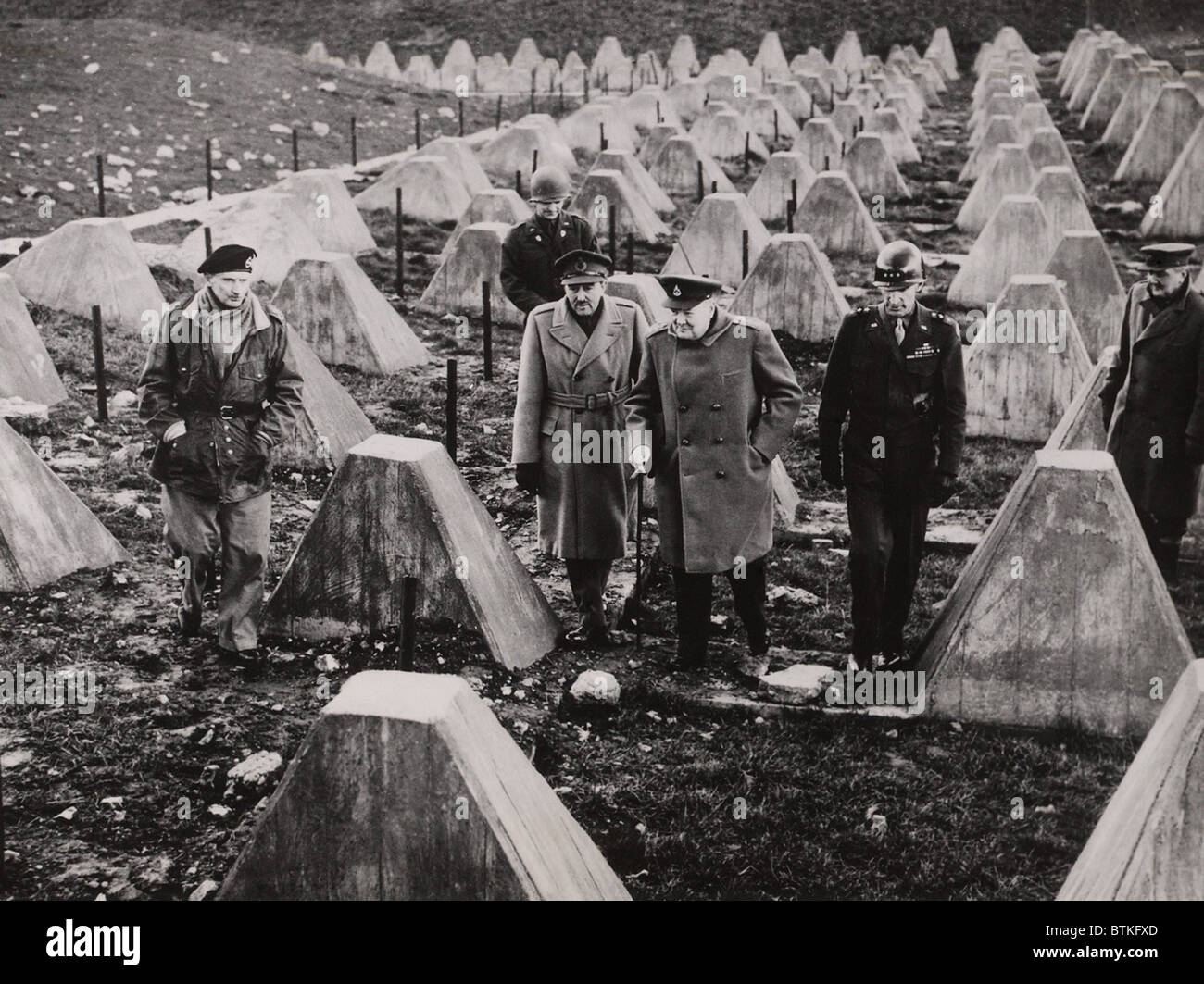 Winston Churchill walks among the dragons teeth (tank traps) of the fallen Siegfried Line. With him are British Field Marshal Montgomery, British Field Marshal Sir Alan Brooke, and U.S. General William H. Simpson. March 1944. Stock Photo