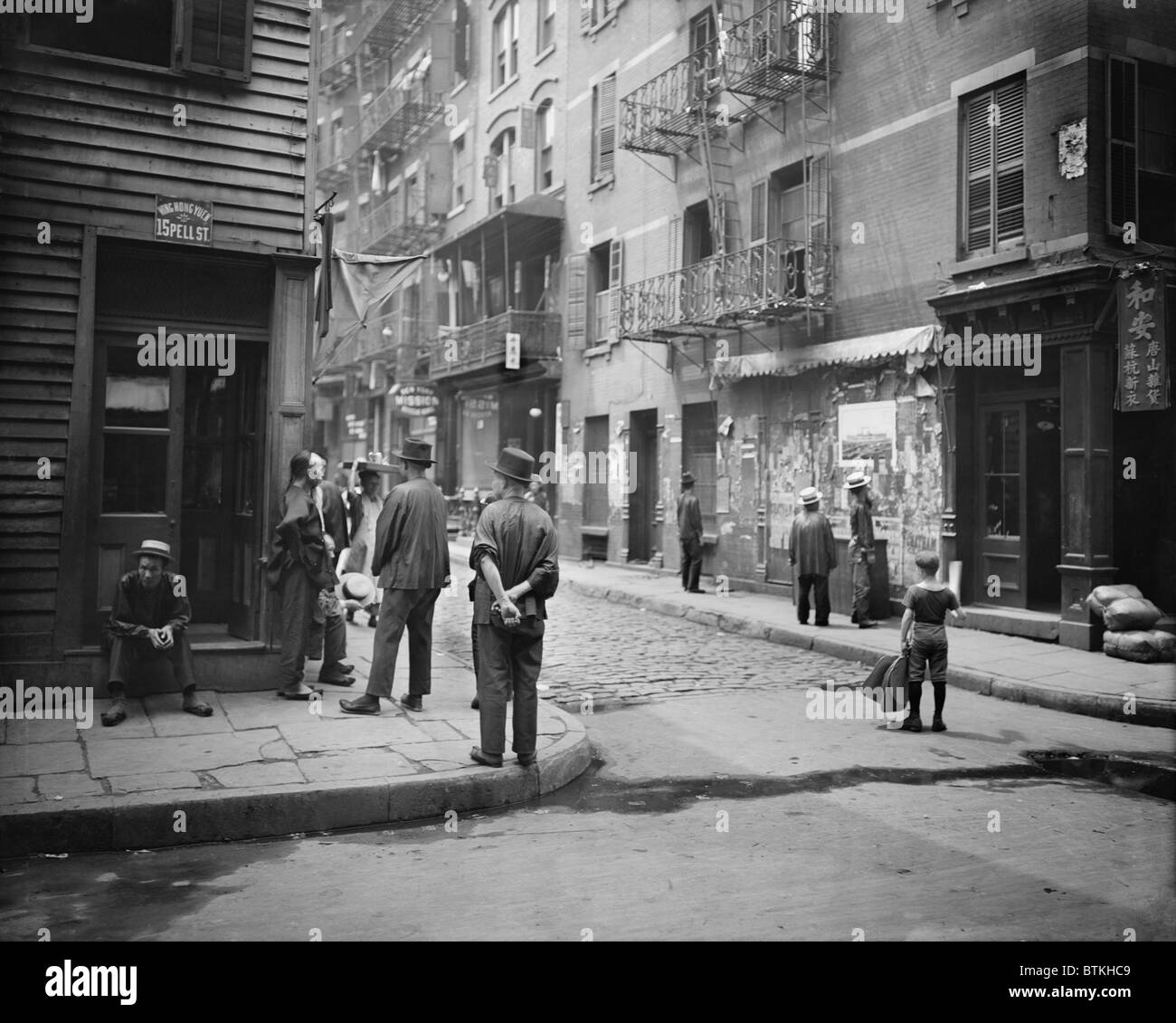 Pell Street in New York City's Chinatown with several Chinese men in traditional dress, one with his hair in the Han Chinese queue, a waist-long, braided pigtail. Ca. 1900. Stock Photo
