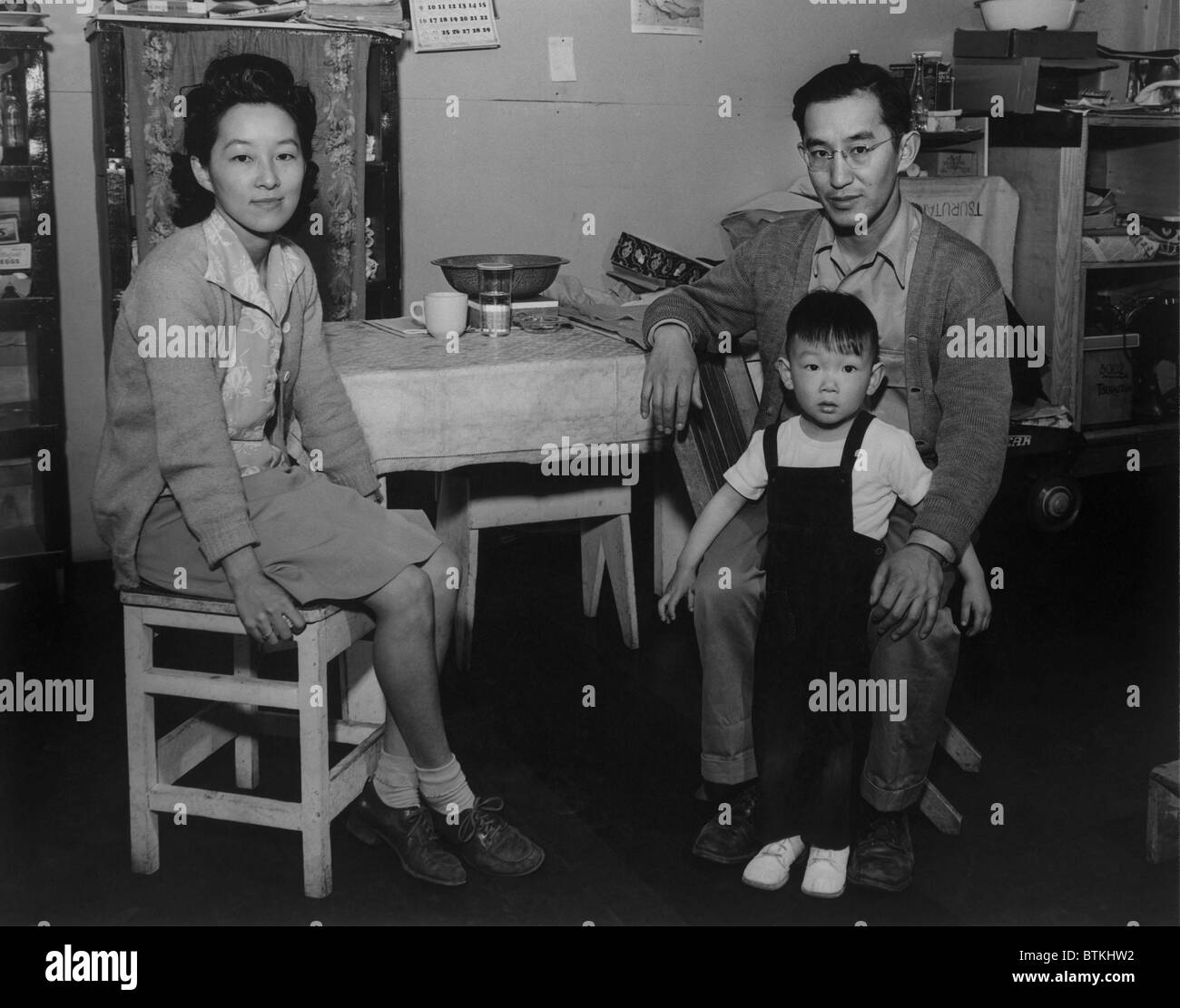Japanese American family interned at Manzanar Relocation Center during World War II. Mr. and Mrs. Henry J. Tsurutani pose in their barracks with their son, Bruce. 1943 photograph by Ansel Adams. Stock Photo