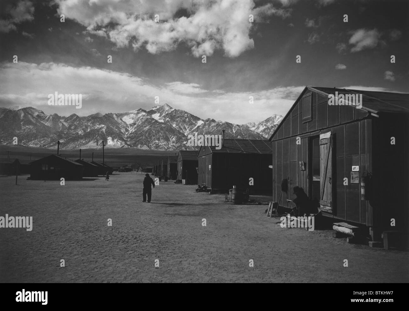 Manzanar Relocation Center, a World War II internment camp for Japanese Americans. A lone man walks on a barracks lined street in the winter of 1943. Photograph by Ansel Adams. Stock Photo