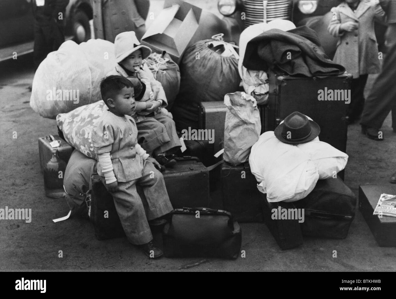 Japanese American children sit among their family's belongings as they wait for transportation to Owens Valley Assembly center for internment during World War II. Los Angeles, California, April 1942. Stock Photo