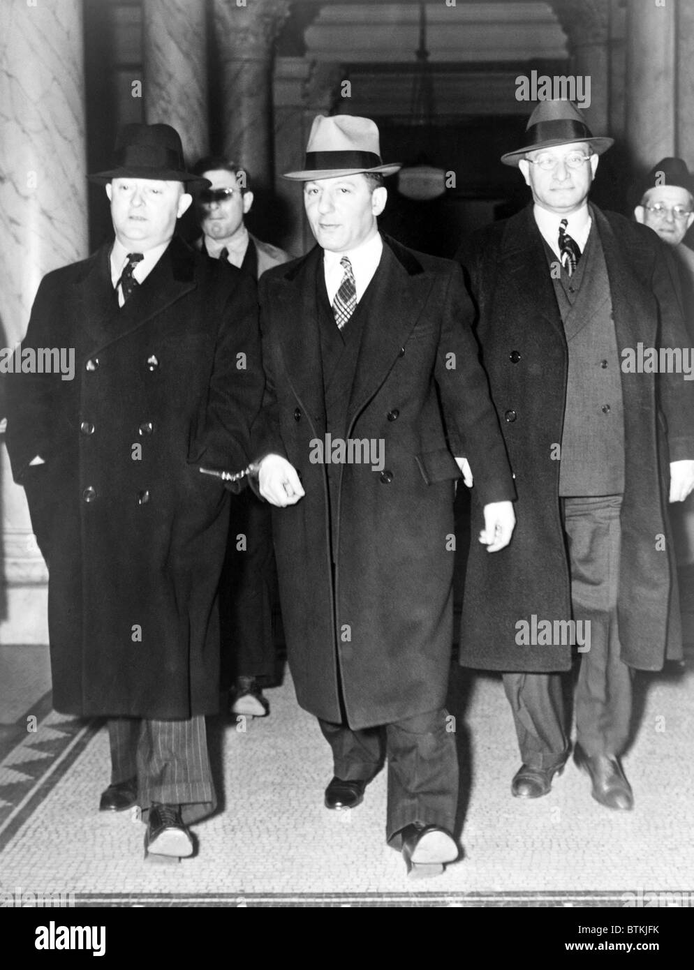 Louis 'Lepke' Buchalter, center, handcuffed to J. Edgar Hoover (left), at entrance to courthouse in New York City in 1939-40. With a $50,000 reward on his head, he was tricked into surrendering to Hoover by a 'friend,' Moey Dimples. Buchalter was executed on March 4, 1944. Stock Photo