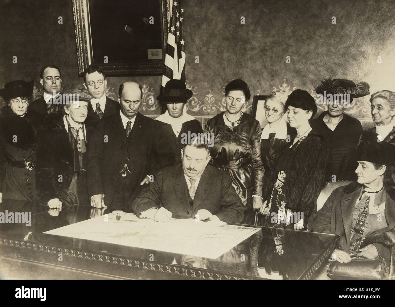 Men and women witness as Colorado governor, Oliver H. Shoup, signs a ratification document for the 19th amendment granting woman's suffrage. Dec. 12, 1919. Stock Photo