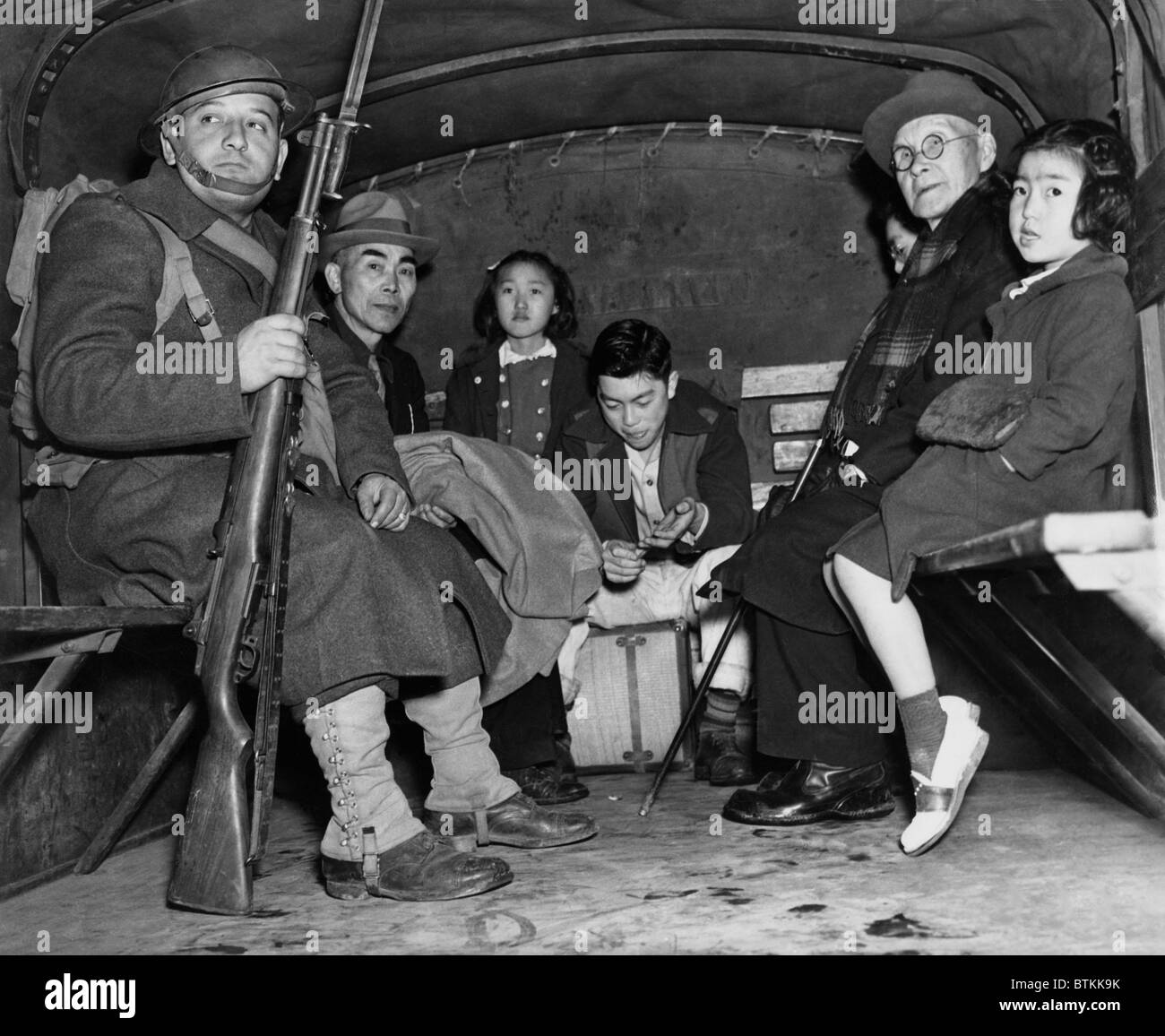 Under armed guard, parentless children and a pastor sit in the back of truck for their evacuation from Bainbridge Island, during the World War II internment of Japanese Americans. The orphans were interned at Manzanar's 'Children's Village,' the only orphanage in internment camps, to which 100 children from Alaska to San Diego were sent for the duration of the war. 1942. Stock Photo