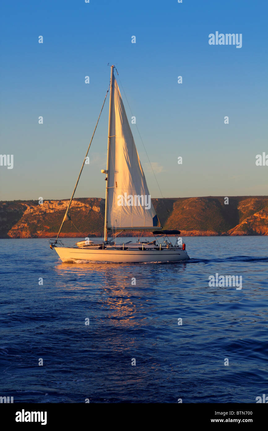 Sailboat sailing golden sunrise in blue ocean sea Stock Photo