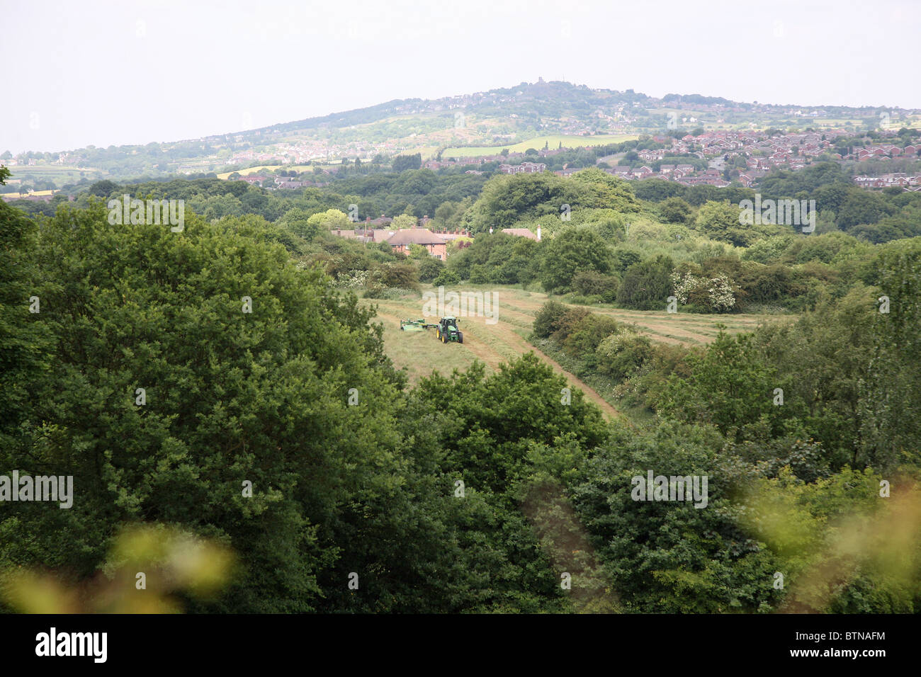 A tractor mowing a grass field with Mow Cop castle folly in the background Stock Photo