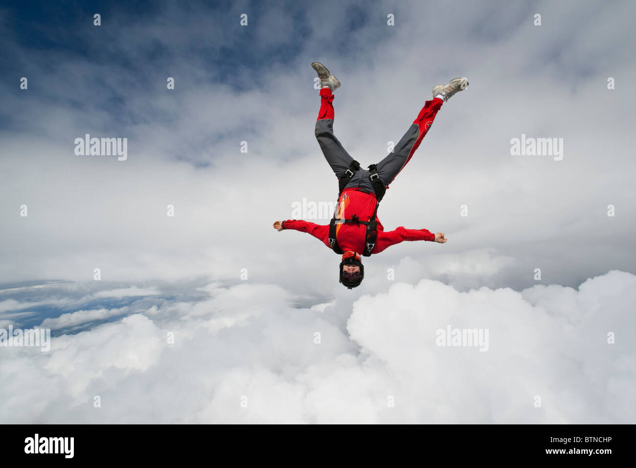 Skydiver man is flying head down within the inverted frog position in between spectacular clouds with over 140 MpH speed. Stock Photo