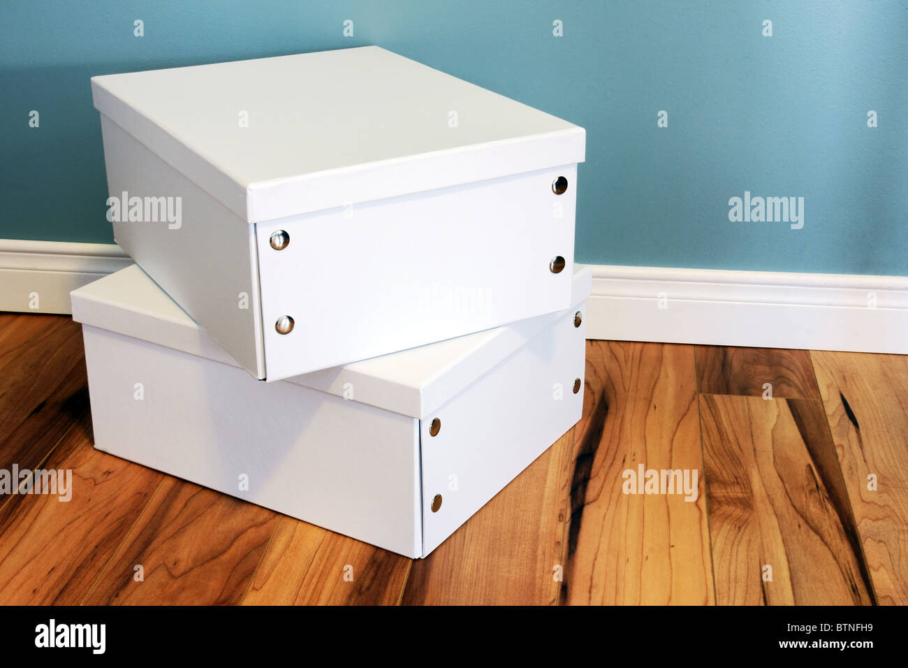 Moving, filing, cleaning: two crisp white cardboard boxes with silver snaps on a wood floor against a blue wall. Stock Photo