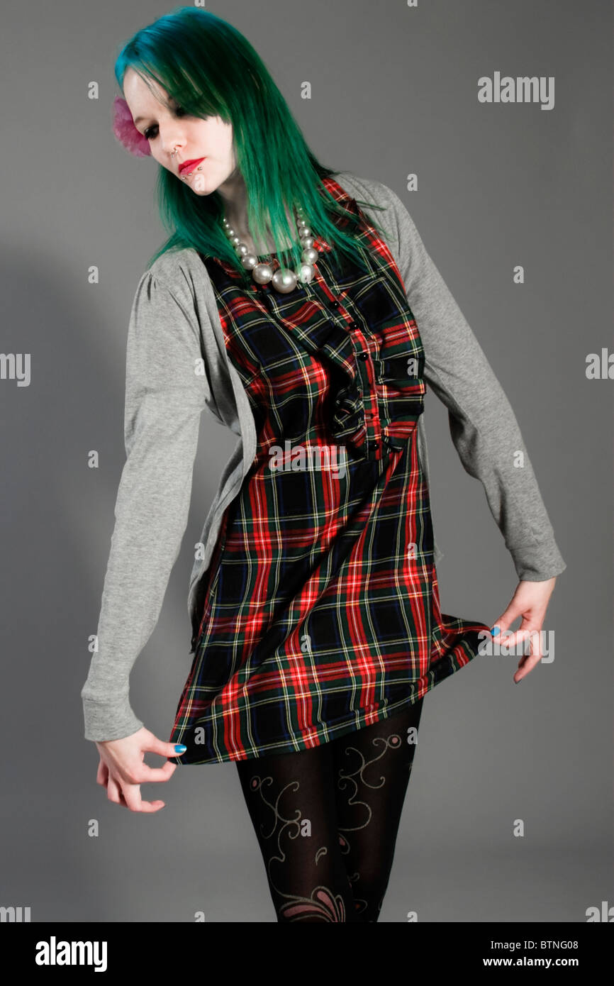 A young goth woman with green hair in a plaid dress and cardigan on a gray background! Stock Photo