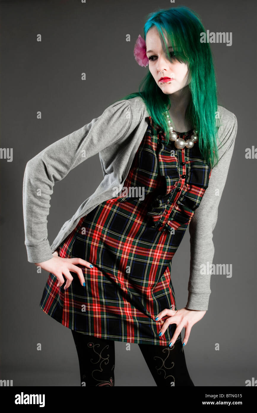 A young goth woman with green hair in a plaid dress and cardigan on a gray background! Stock Photo