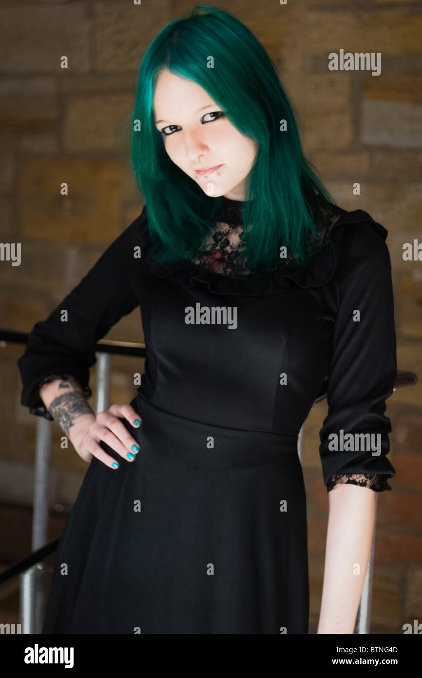 A young goth woman with green hair wearing a green dress and standing in a fire escape. Stock Photo