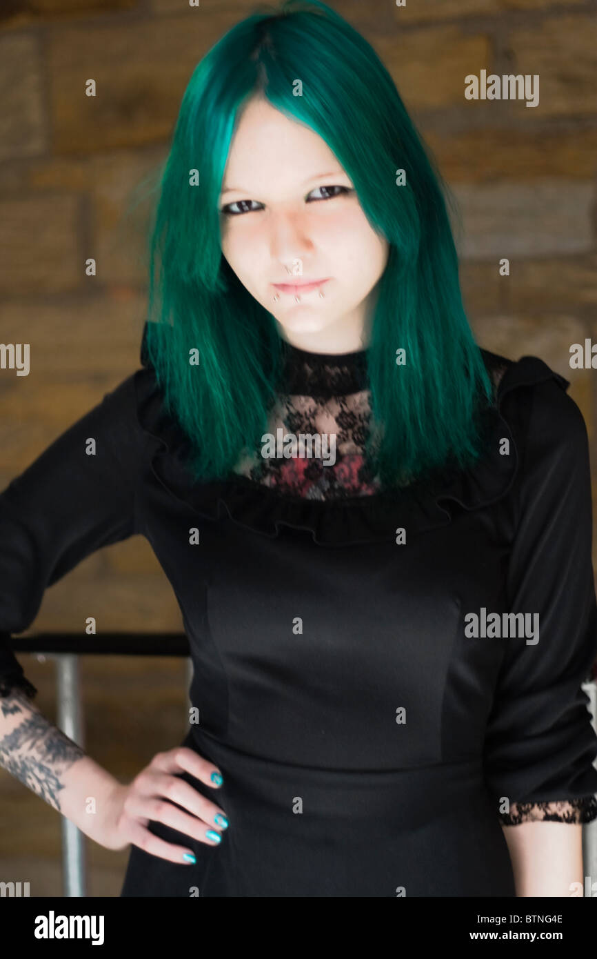A young goth woman with green hair wearing a green dress and standing in a fire escape. Stock Photo