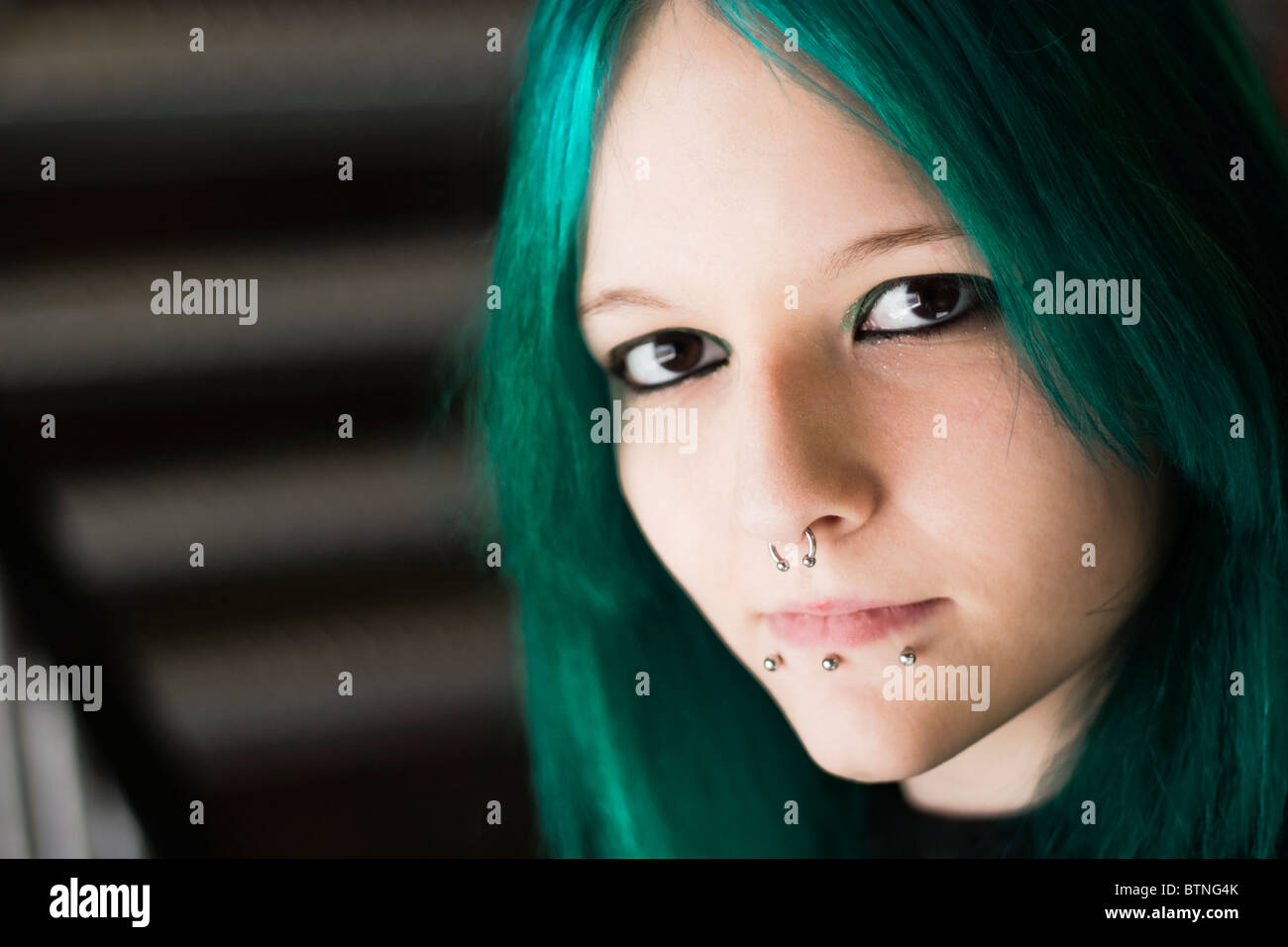 A young goth woman with green hair wearing a green dress and standing