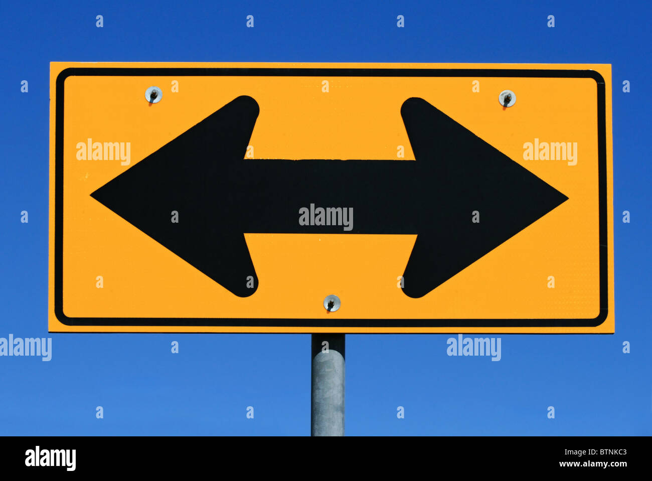 two sided black and yellow road sign designating two way traffic with a blue sky background Stock Photo