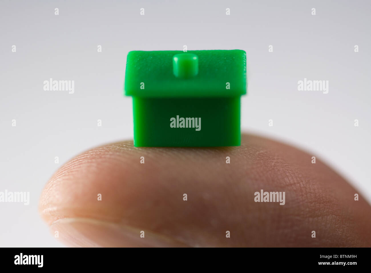 Monopoly house balanced on the thumb. Stock Photo