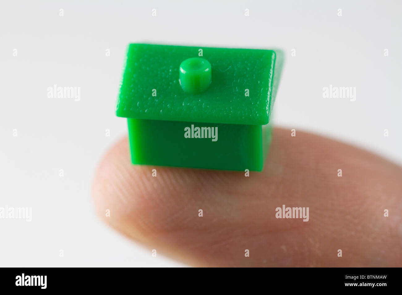 Monopoly house balanced on the finger. Stock Photo