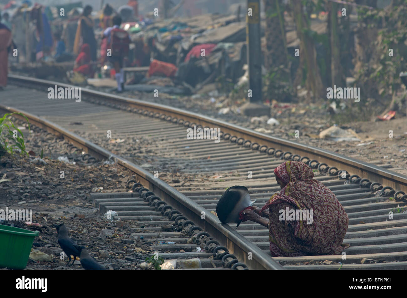 Old woman cleaning a cooking pot on railway tracks near Kumartuli, Kolkata (Calcutta), West Bengal, India Stock Photo