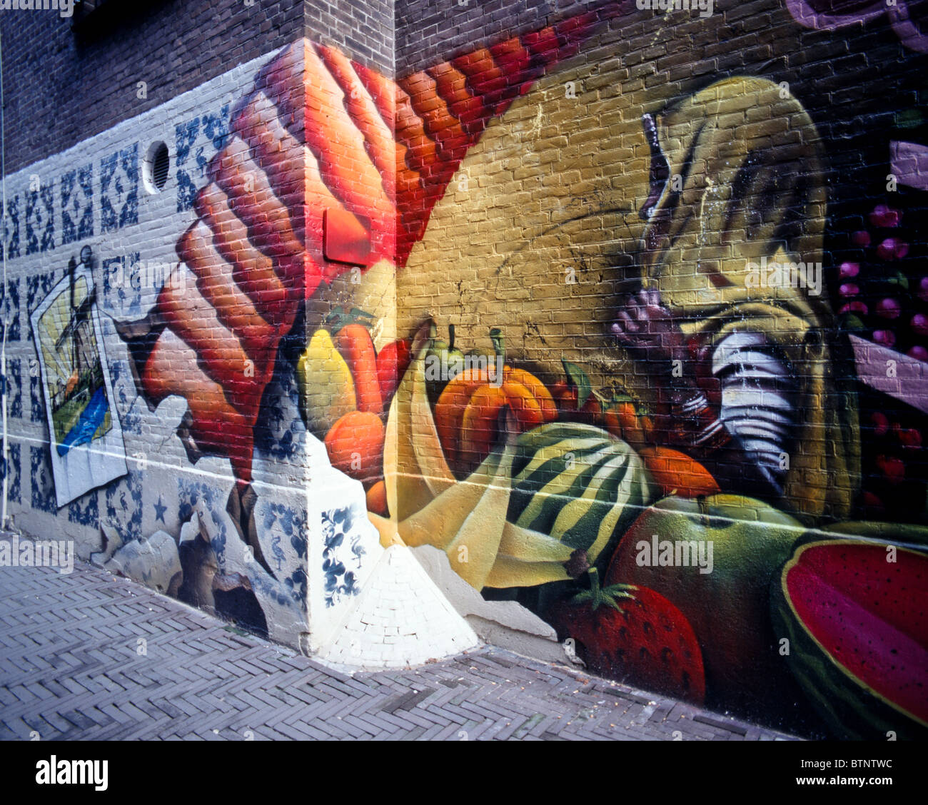 Graffiti on a brick wall of fruits & vegetables and a dark skinned woman with a scarf in a narrow alley, The Hague, Netherlands Stock Photo