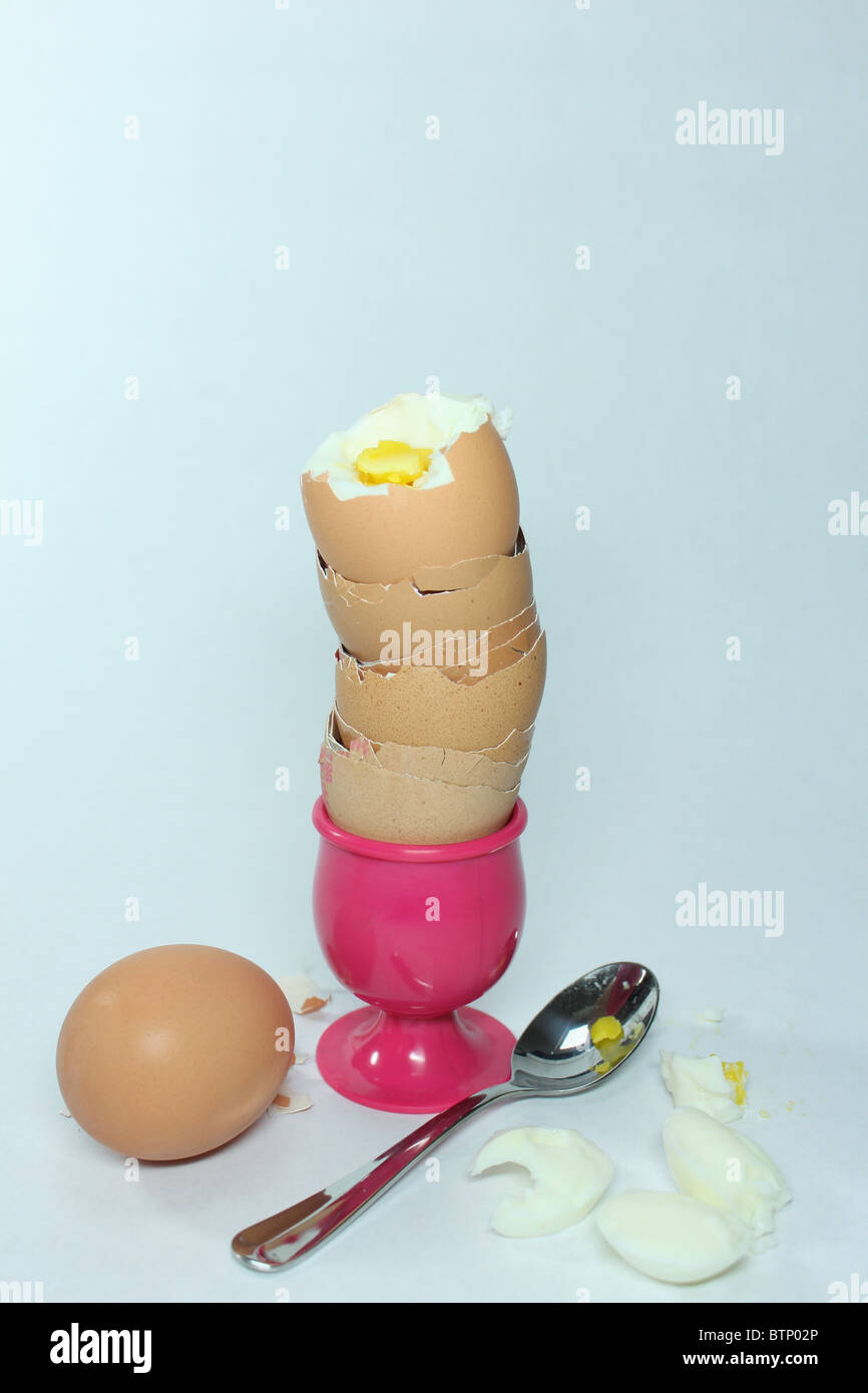 boiled egg on stack of empty egg shells in pink egg cup with spoon and  whole boiled egg Stock Photo