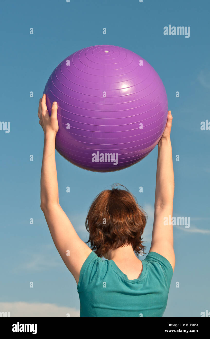 Young Woman Holding a Big Fitness Ball over her head Stock Photo