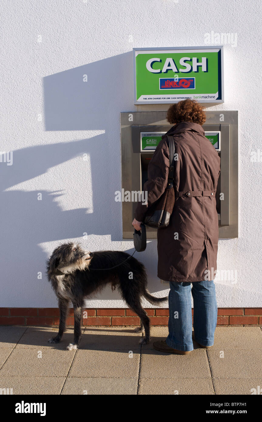 Woman with pet dog making cash withdrawal at ATM Stock Photo