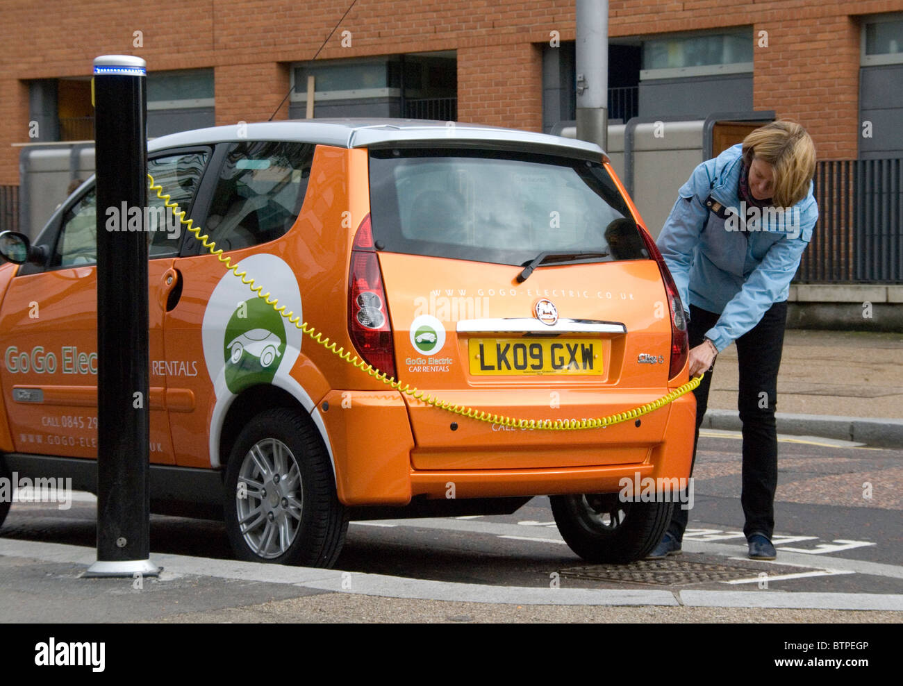 Woman plugging in electric vehicle EV at free EV parking bay South Bank London UK GoGo Electric Vehicle rentals Stock Photo