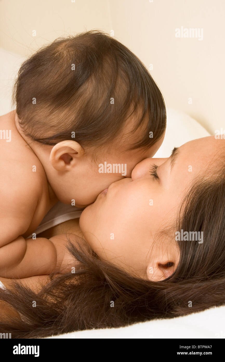 Mom and son lying down on bed and mother kissing the infant baby Stock Photo