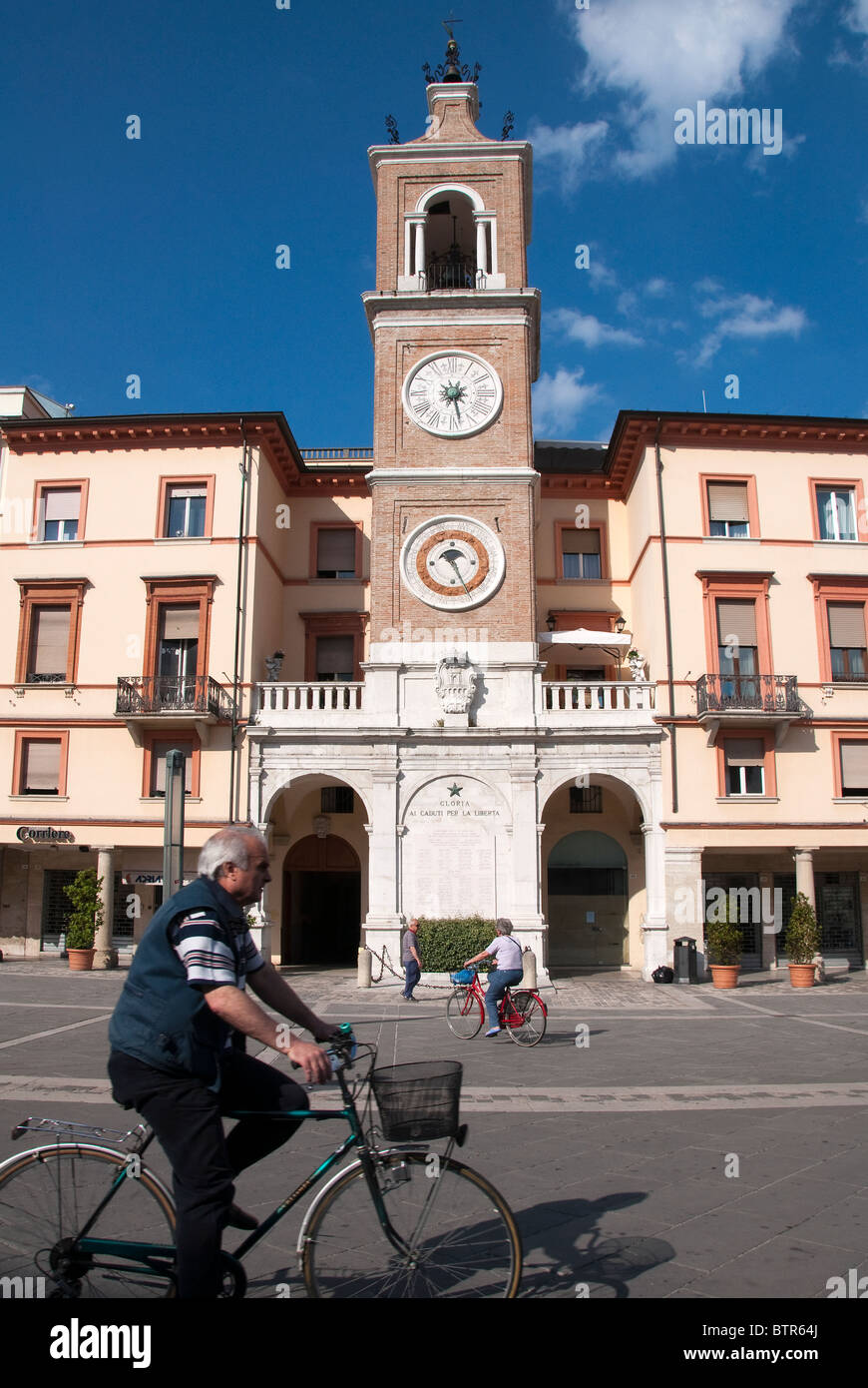 Man cycling past Clock tower telling the time, date and Zodiac sign in Piazza Cavour, Rimini, Emilia Romagna, Italy Stock Photo