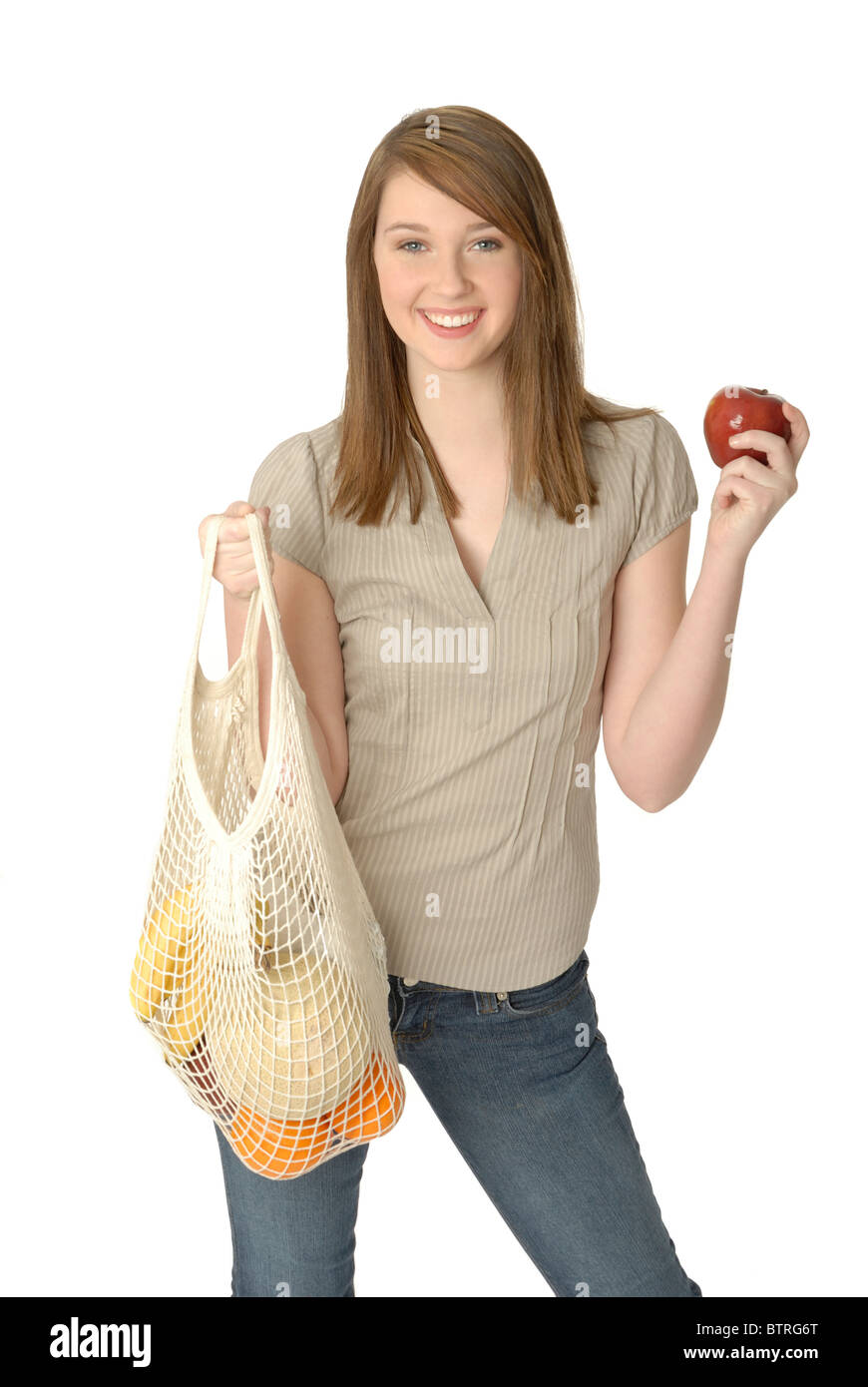 Young woman with environmentally-friendly reusable string shopping bag filled with fresh fruit, holding an apple. Stock Photo