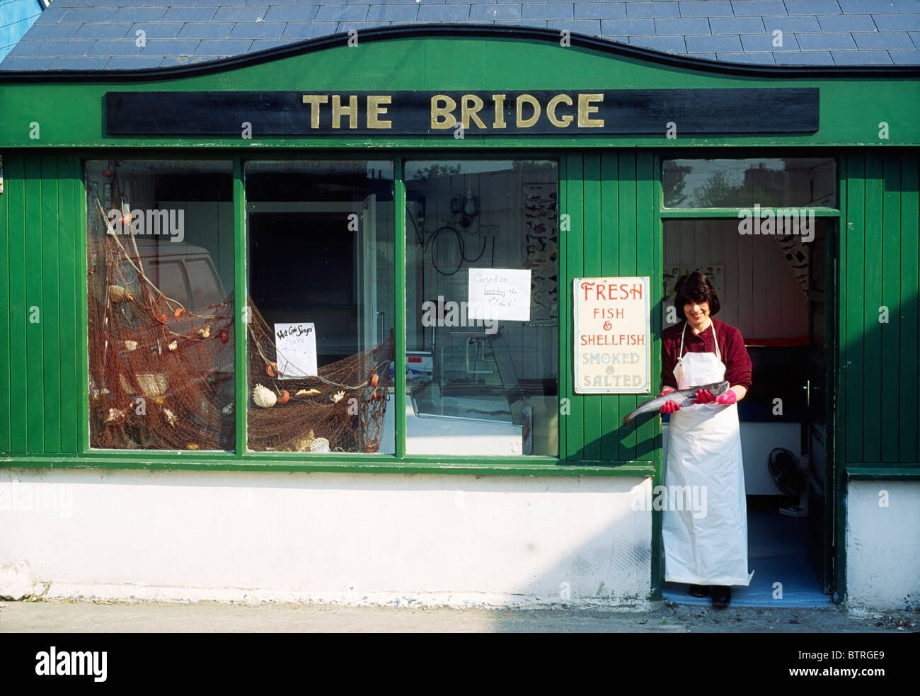 The Bridge, Skibbereen, Cork, Ireland; Woman Standing Outside Of A Fish Shop Stock Photo