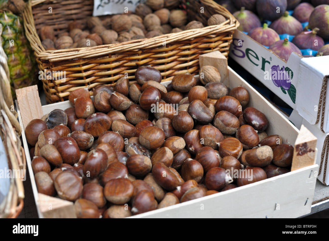 A box piled up with chestnuts ready for roasting on an open fire, a box of luxury figs and a basket of walnuts on a market stall Stock Photo