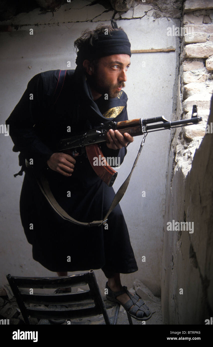 foreign mujahideen fighter in Kabul Afghanistan holding Kalashnikov AK47 assault rifle looking out through tank shell hole wall Stock Photo