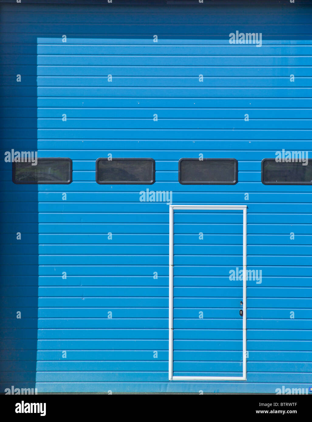 Blue metal shutter door with another smaller door and small windows embedded.  Depth due to shadows. Stock Photo