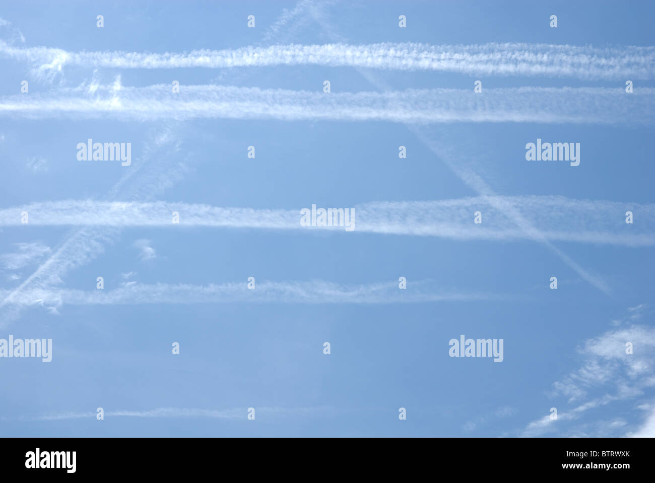 Several contrails forming a nearly graphical pattern in otherwise clear and blue sky.  Condensation Trails from dens air traffic Stock Photo