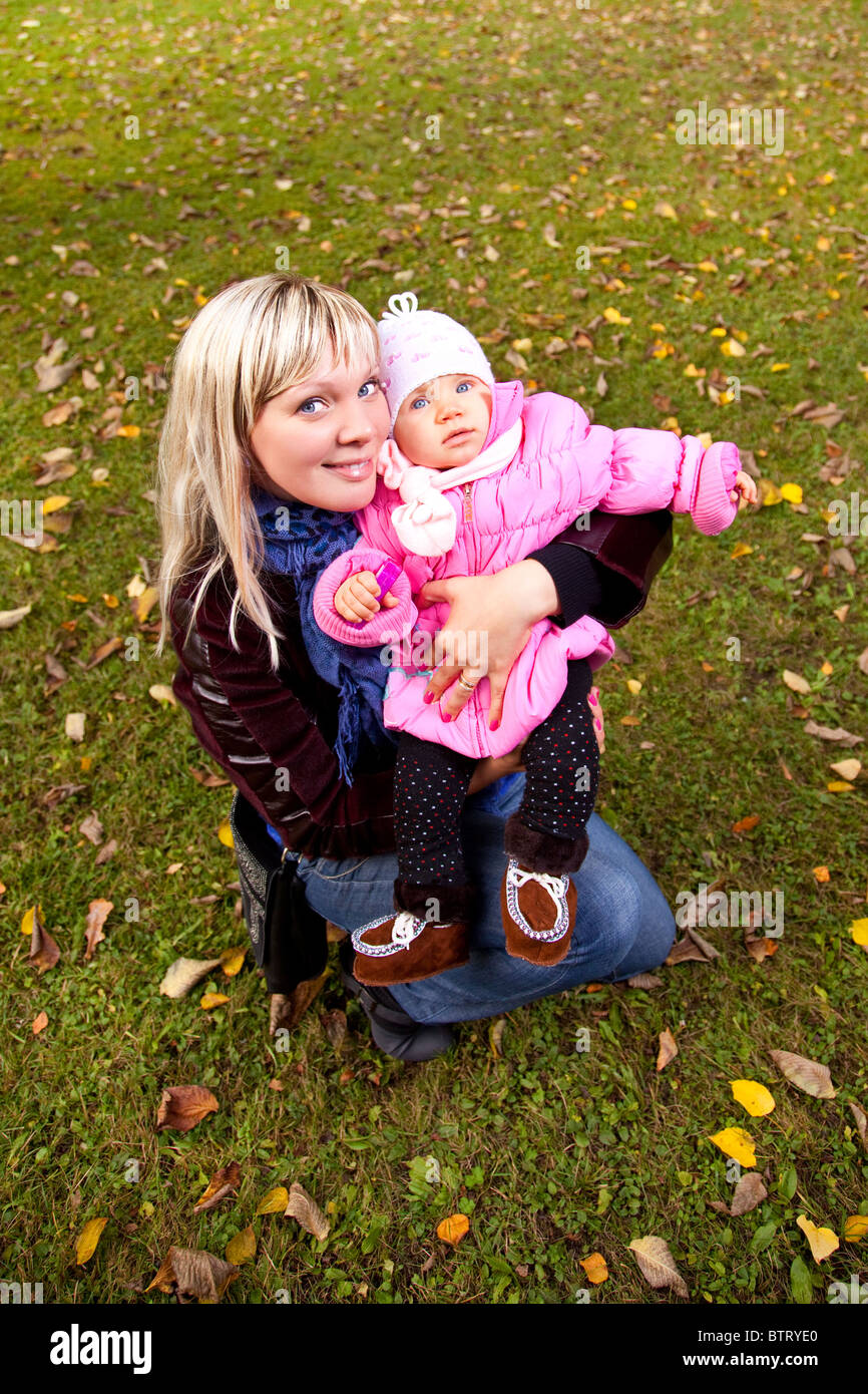 Young mother and little child siting on grass in autumn park. Stock Photo