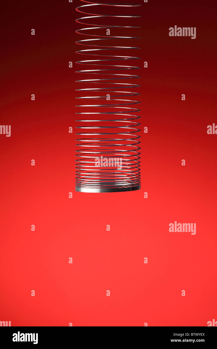 A silver metal spring stretching downwards. Red colored background Stock Photo