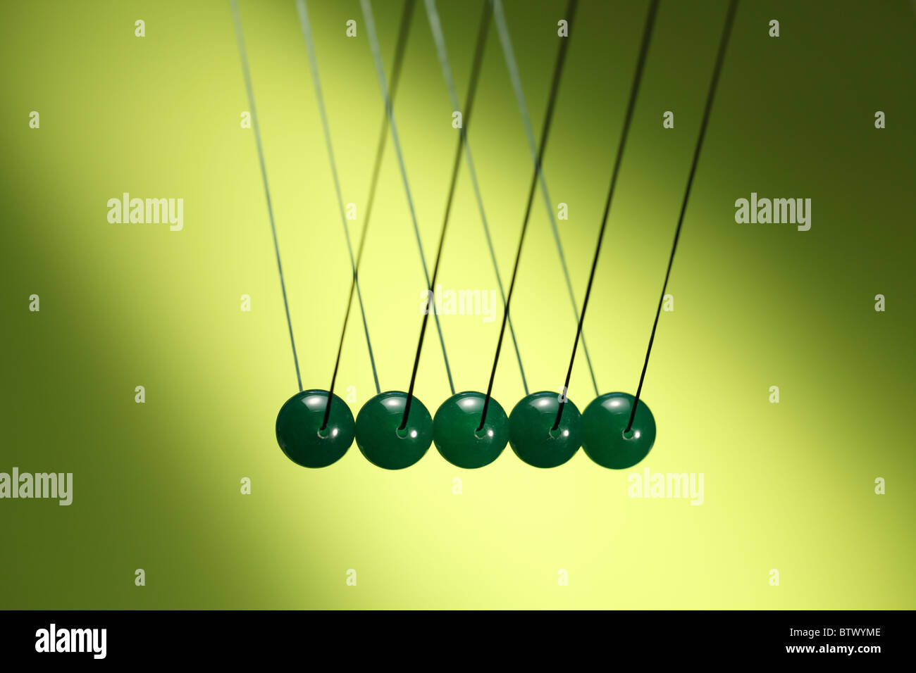 Five green marbles in row hanging from string. Illustrates Newton's cradle, a device that demonstrates conservation of momentum. Stock Photo