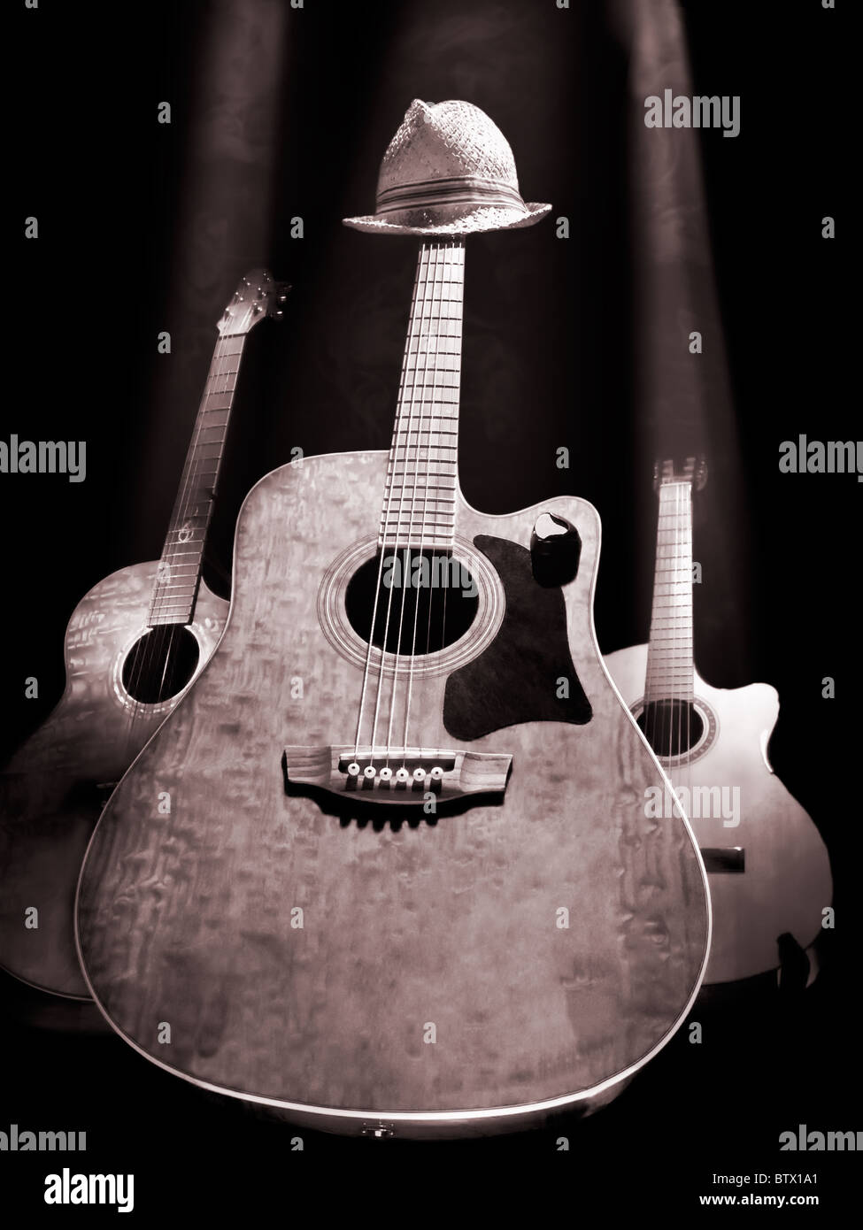 three acoustic guitars on the stage lit with the overhead lights , black and white photo Stock Photo