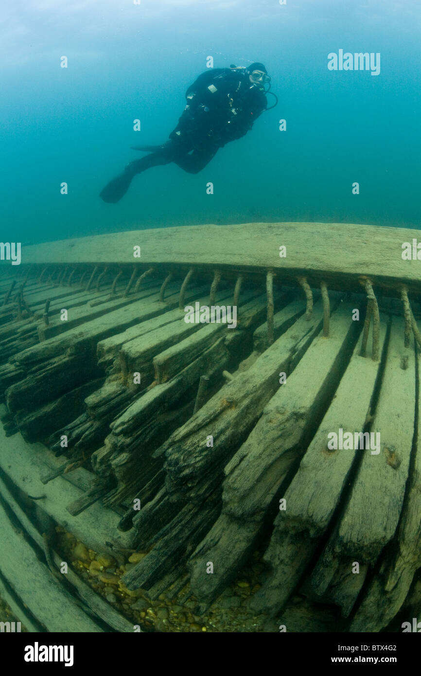 A diver swims above the wooden hull of a shipwreck on the bottom of