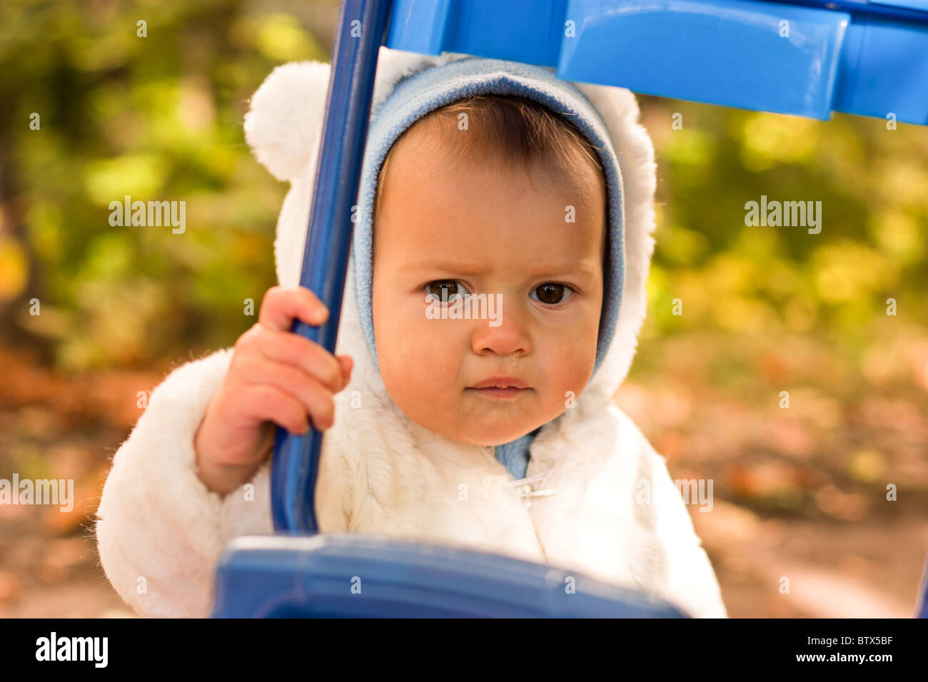 Beautiful baby girl in white jacket looking into the blue bike frame