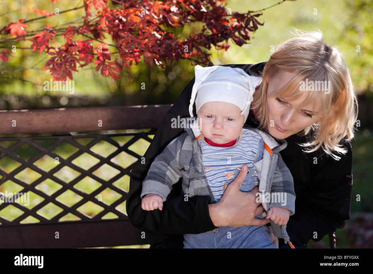 Mother holding her baby boy on the bench in the autumn garden. Stock Photo