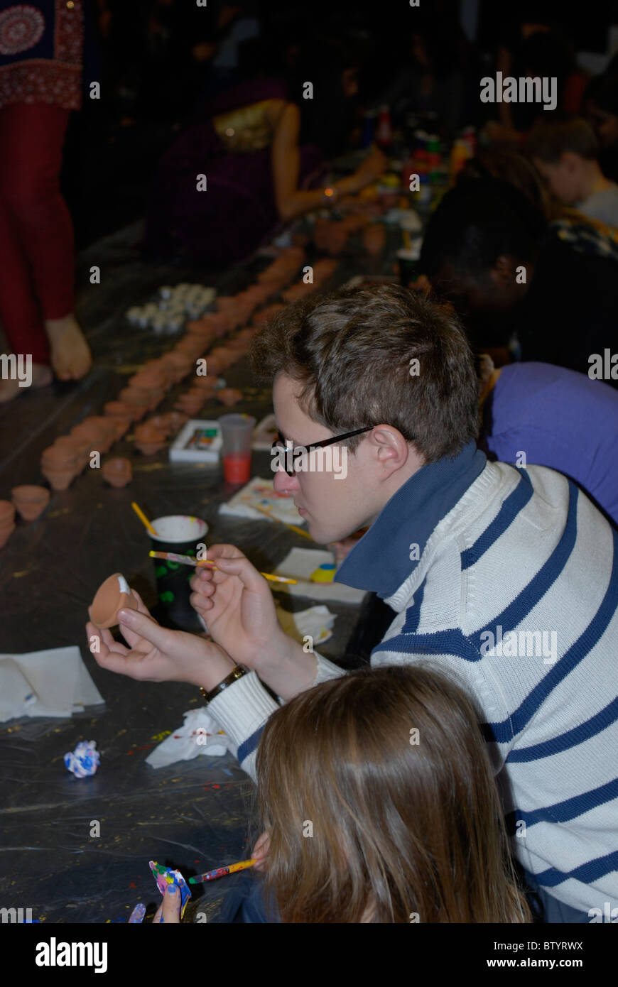 People painting small clay pots for candles at a community festival