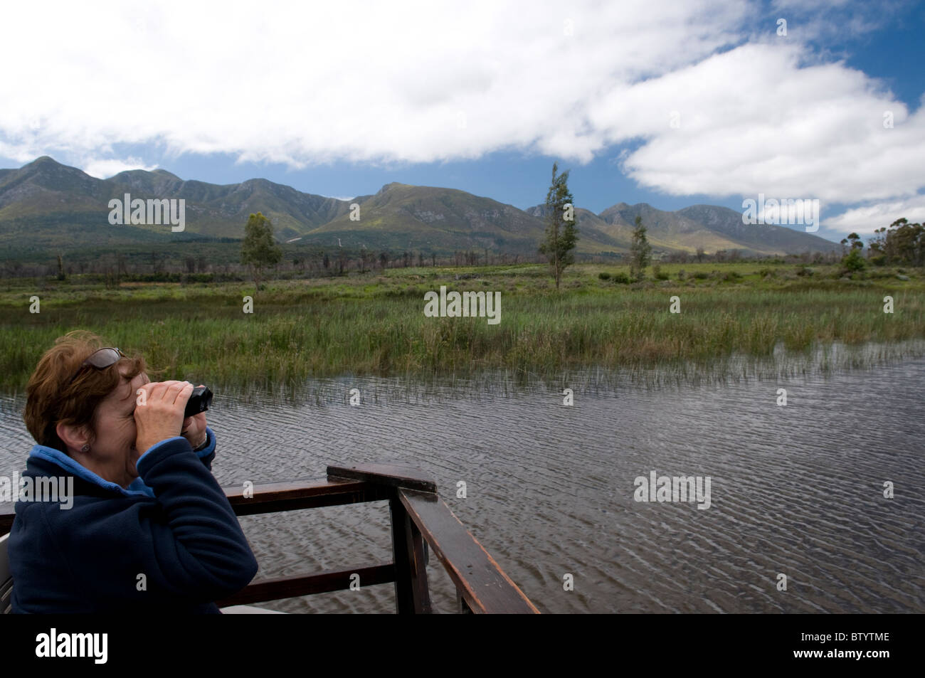 Woman sitting on a viewing area and looking through binoculars Stock Photo