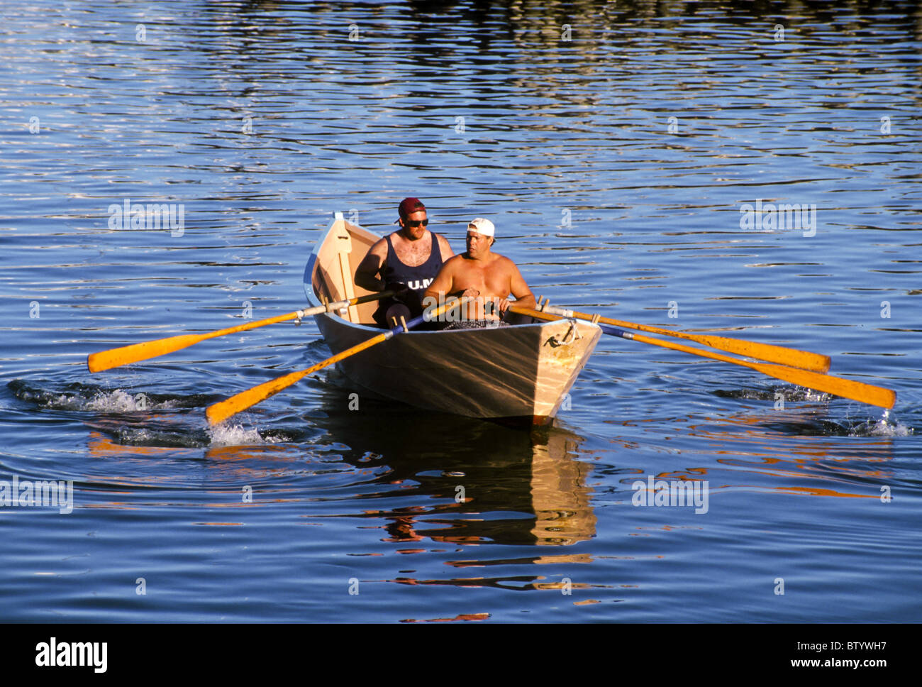 Two men rowing a traditional wooden dory in Gloucester Harbor Stock