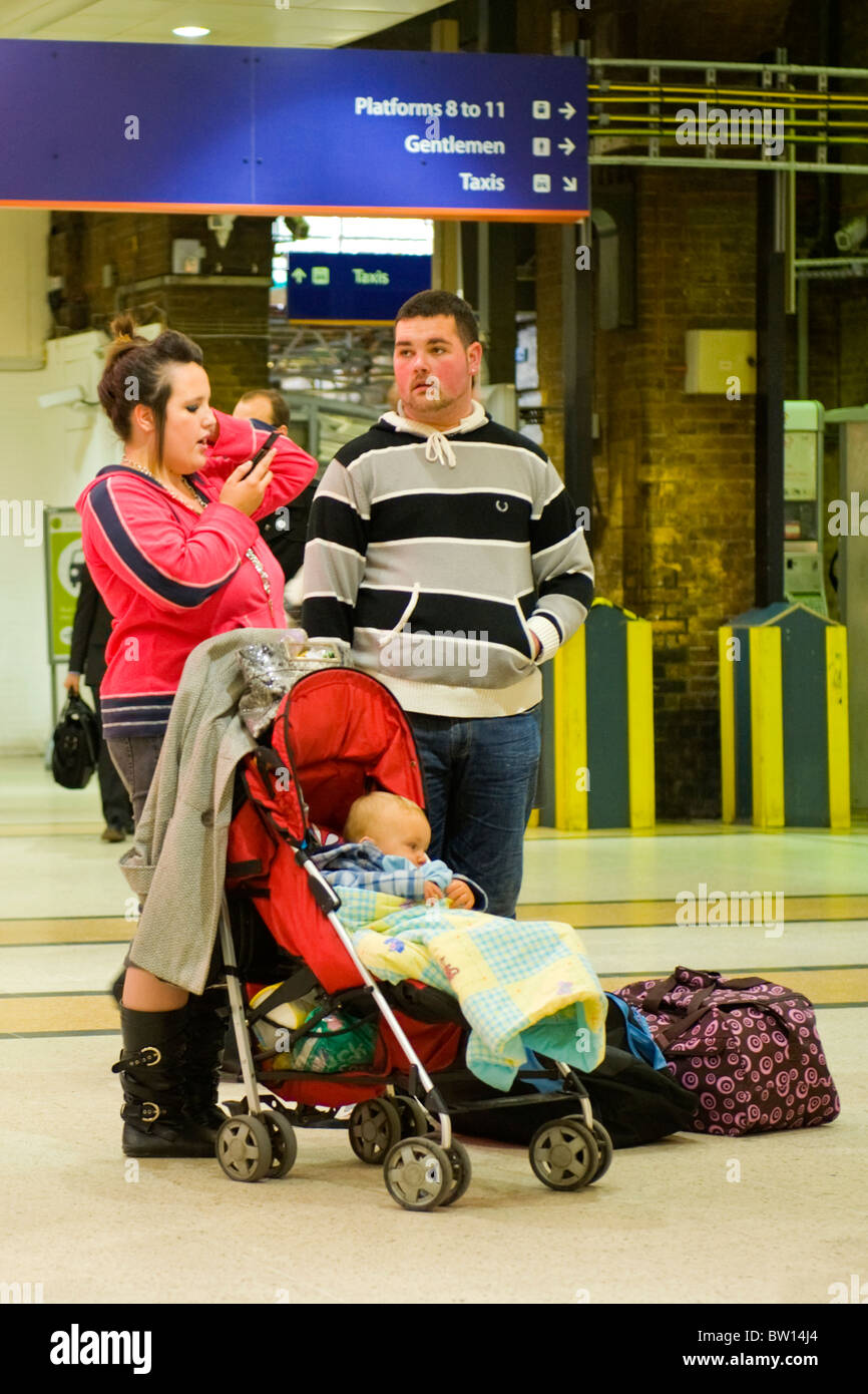 Kings Cross Station family typical young mother on mobile cell phone father unshaven jeans baby in pushchair waiting for train platform Stock Photo