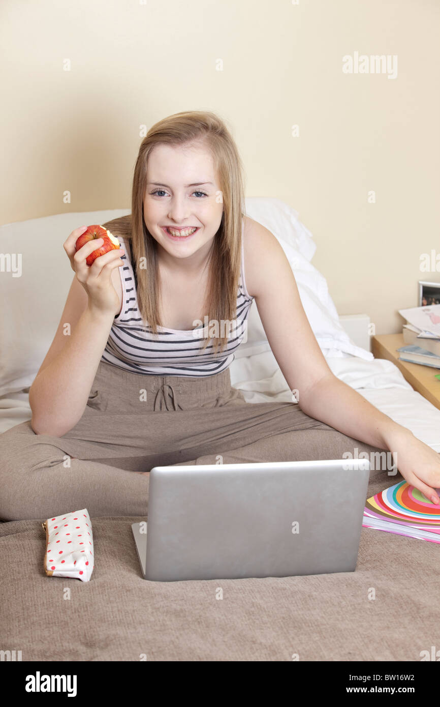 A teenage girl eats an apple whilst studying in her bedroom UK Stock Photo