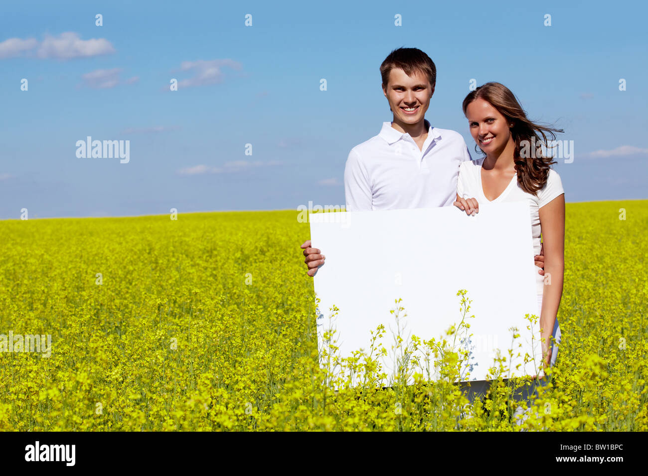 Portrait of happy young couple with blank paper standing in meadow Stock Photo